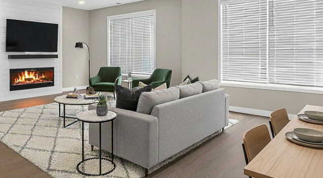 Modern living room with gray sofa, green chairs, fireplace, and large windows.