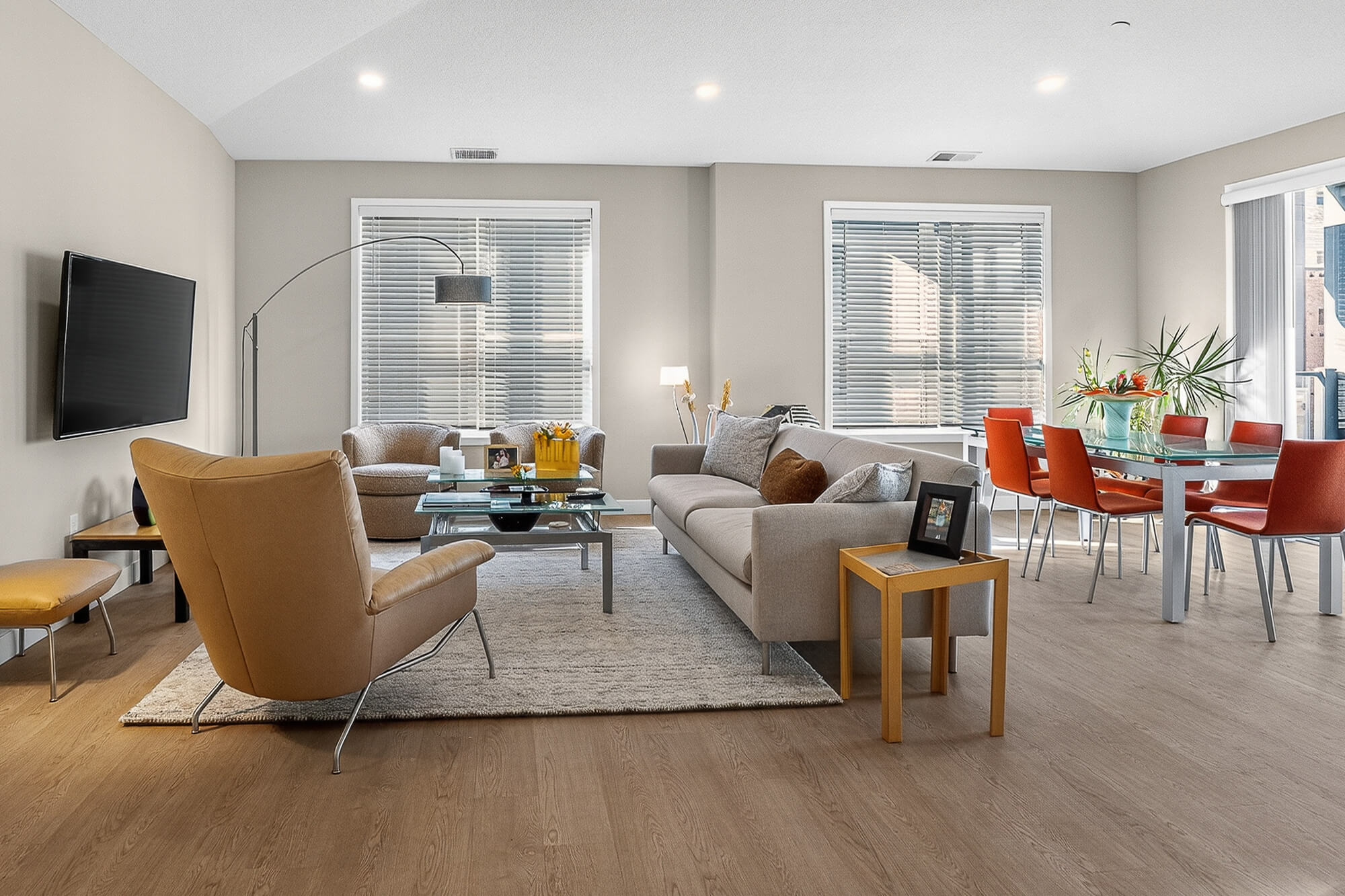 Modern living room with beige furniture, wooden floors, and red dining chairs.